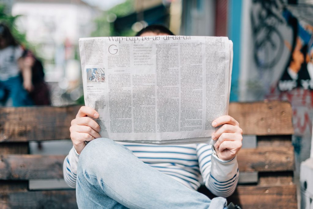 Person sitzt auf einer Bank und liest eine Zeitung.